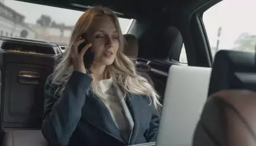 woman looking at laptop and on phone in back seat of town car, a successful management training program graduate